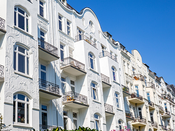 Weißer Altbauimmobilienkomplex mit Balkonen und blauem Himmel